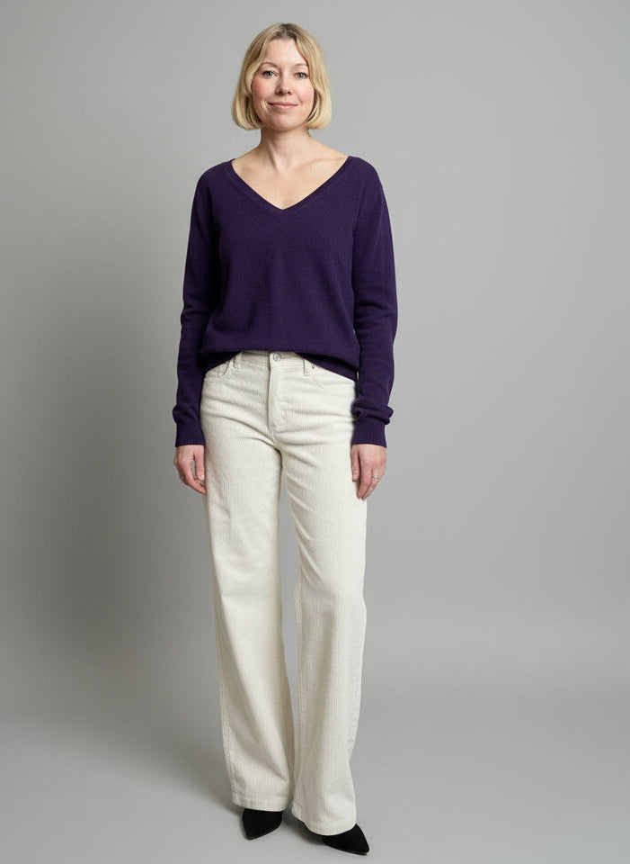 Woman standing in a clothing store with racks of clothes and a pink sweatshirt in the background.