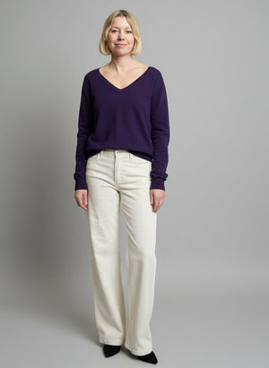 Woman standing in a clothing store with racks of clothes and a pink sweatshirt in the background.